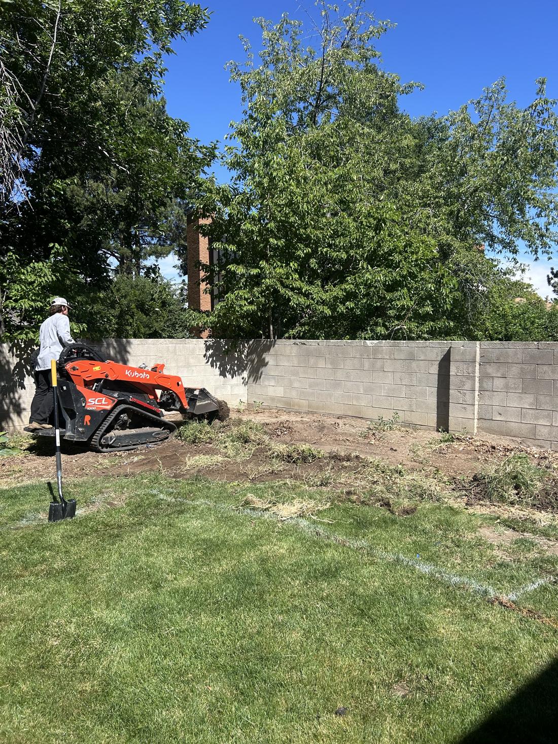 Track loader stripping old sod along a block wall