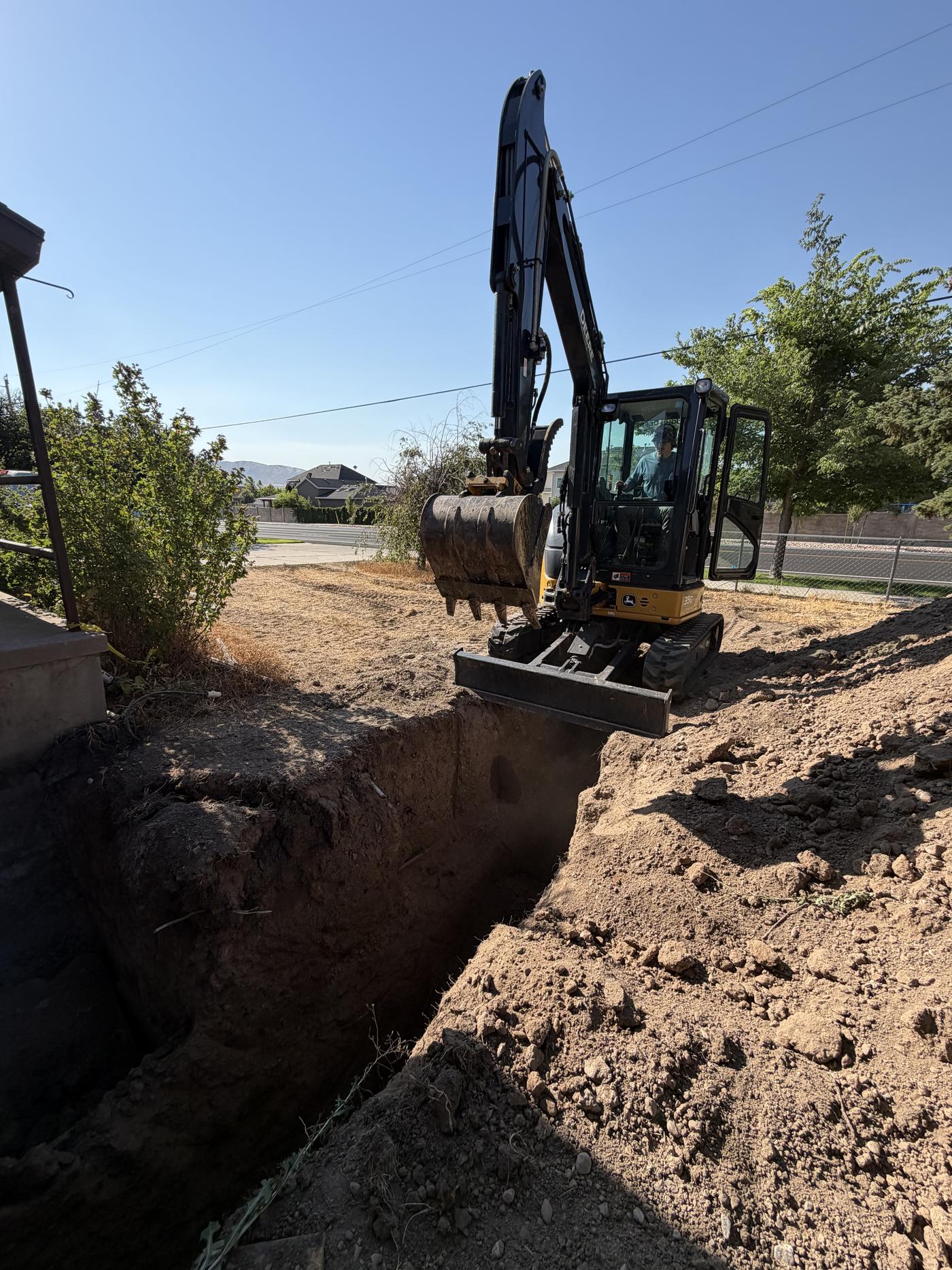 Excavator digging a drainage trench beside a home