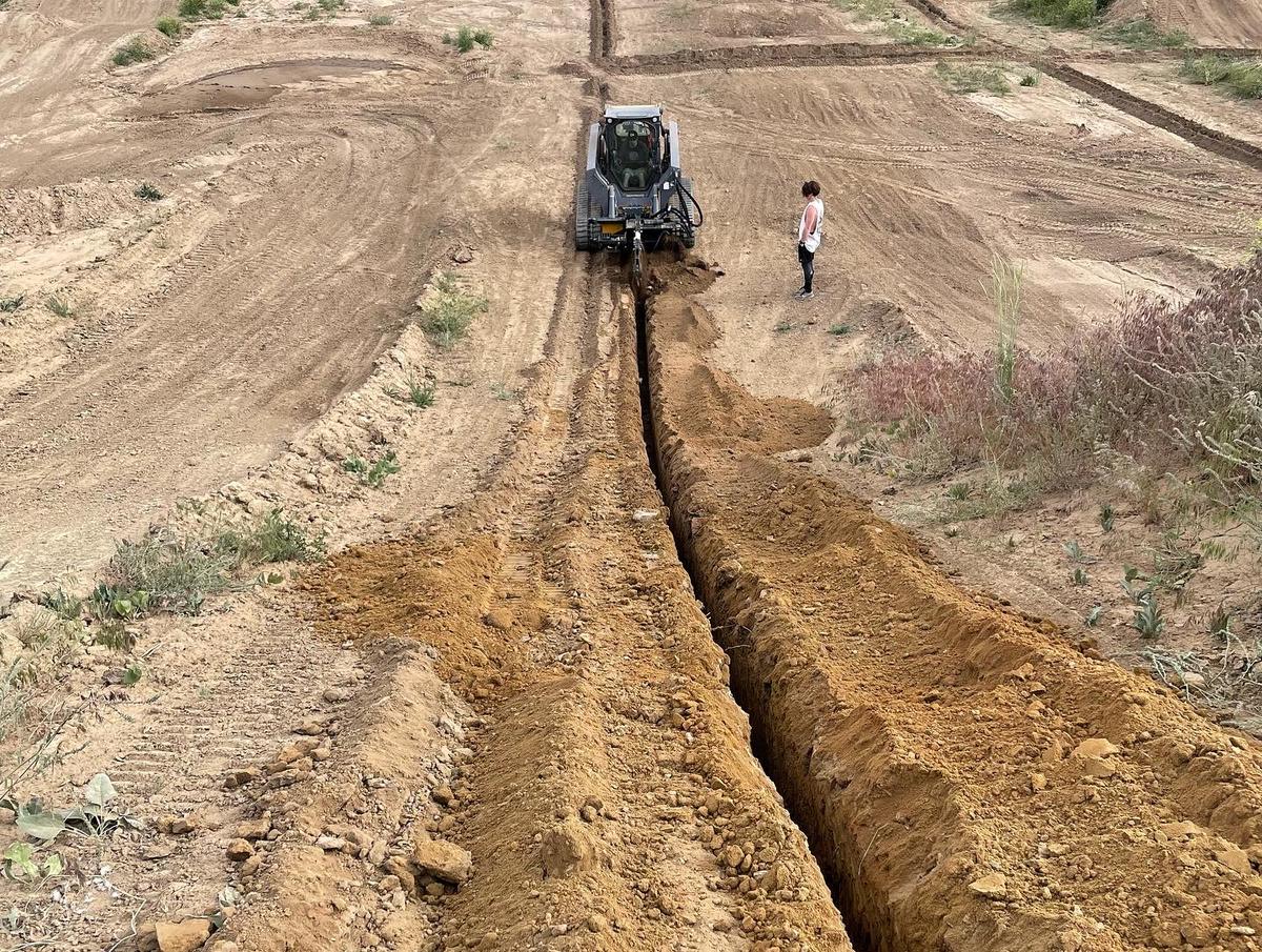 Track loader cutting a long utility trench across a graded lot